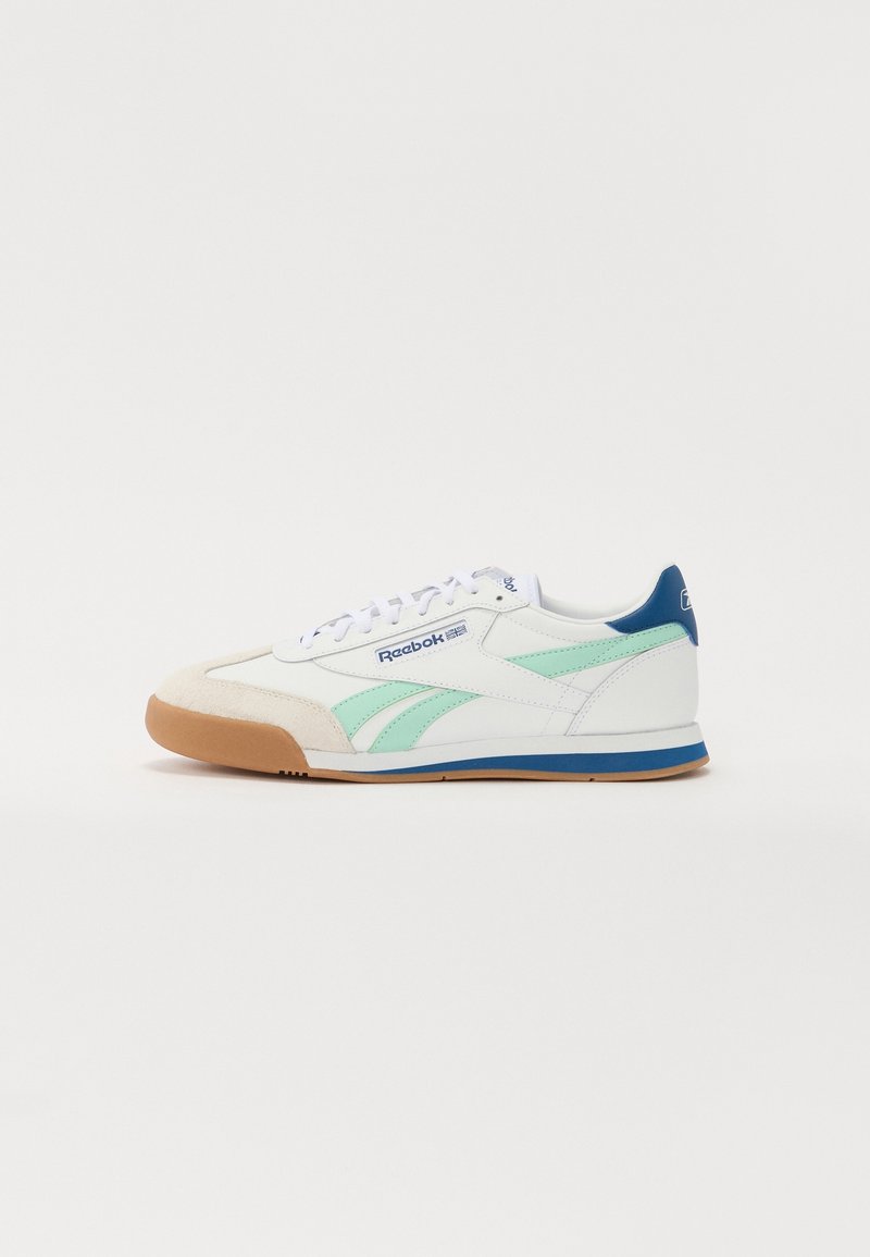 Baskets blanches Reebok avec des bandes bleu sarcelle, un bout beige, des touches bleues au talon et à la semelle, et des lacets blancs, présentées sur un fond uni.