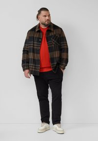 Ruuduline särk musta ja pruuni, punane dressipluus all, mustad püksid ja beežid spordijalatsid. Jakk on nööpidega kinni ja sellel on rinna tasku.