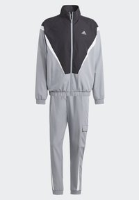 Chándal gris con acentos negros, con cuello alto, cremallera completa, puños elásticos y bolsillo tipo cargo en los pantalones. Fabricado con material ligero.