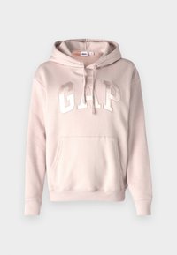 Sudadera color rosa empolvado hecha de una tela suave, cuenta con un bolsillo canguro al frente, capucha con cordones y un logo "GAP" en relieve en blanco.