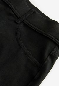 Pantalones de mezclilla negros con una textura suave, corte recto y detalles de costura en la cinturilla y los bolsillos.