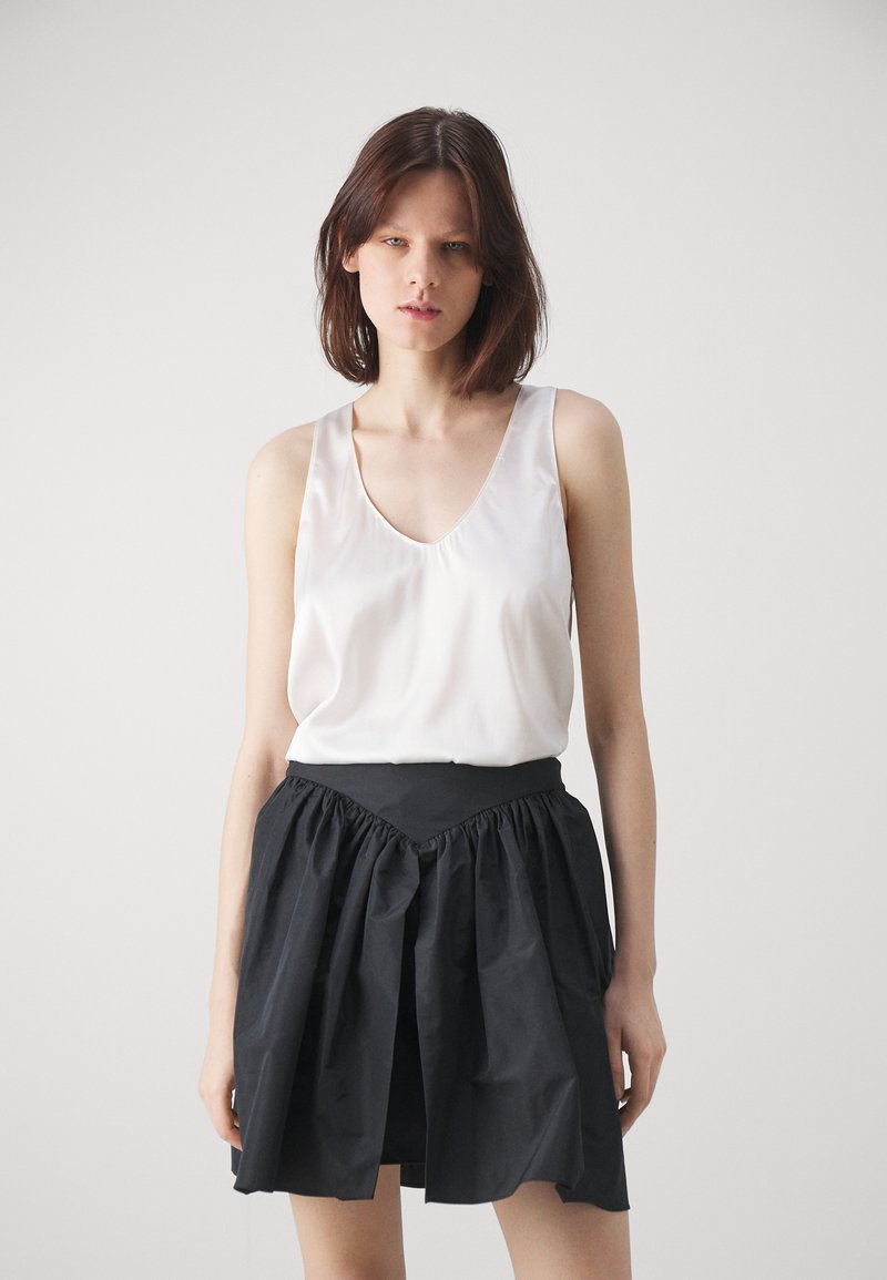 Top in satin bianco con scollatura a V profonda abbinato a una gonna nera arricciata, caratterizzata da una vita strutturata e una texture a strati.