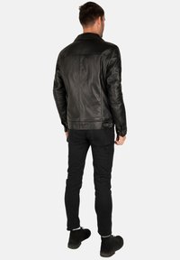 Giubbotto di pelle nera con colletto, texture liscia e design aderente. Presenta dettagli di cucitura e un accento con fibbia laterale.