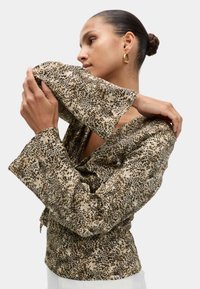 Blusa a maniche lunghe in tessuto beige con stampa animale nera. Presenta un profondo scollo a V e maniche larghe e svasate. Texture liscia.