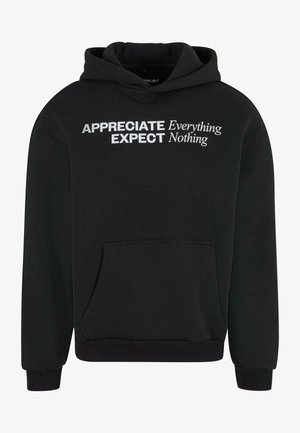 Sort hættejakke med en front kangaroo-lomme og hvid tekst: "SÆT PRIS PÅ ALT, FORVENT INTET." I 100% bomuldsmateriale, lange ærmer og justerbar hætte.