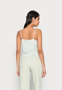 Camisola de alças fina em tie-dye verde claro, com uma silhueta ajustada e uma textura suave. Combinada com calças de corte direito verde claro.