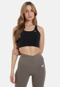 Zwarte crop top met een ronde halslijn, gecombineerd met hoge olijfgroene leggings met een wit logo en een gladde, matte textuur.