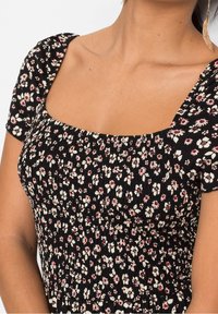 Černé květinové šaty s čtvercovým dekoltem, krátkými nabíranými rukávy a smockovaným živůtkem. Obsahují malé bílé a červené květiny na tmavém pozadí.