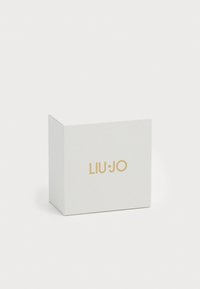 Scatola bianca con superficie testurizzata e motivo geometrico, logo dorato "LIU-JO" sul davanti, apertura superiore e bordi angolari.