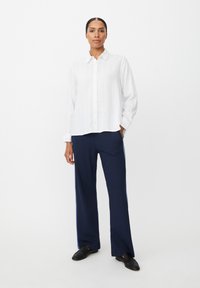 Biała koszula na guziki z pionowymi paskami, w zestawie z luźnymi granatowymi spodniami z bocznymi paskami. Całość dopełniają płaskie czarne buty.