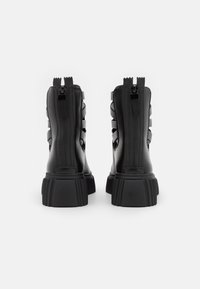 Czarne botki za kostkę z grubą, żebrowaną podeszwą, ze skórzanego materiału, z podwójnym zamkiem błyskawicznym i wycięciami po bokach dla wentylacji. Gładka faktura.