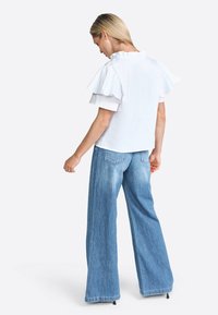 Blusa bianca a balze con colletto alto abbinata a pantaloni larghi in denim azzurro chiaro, a vita alta, con orli sfrangiati e tasche posteriori.