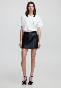 Witte t-shirt met een rhinestone zakdetail, gecombineerd met een zwarte leren miniskirt en zwarte hakken met strikaccenten.