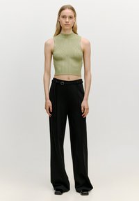 Hellgrünes, geripptes Strick-Crop-Top mit hohem Kragen, kombiniert mit schwarzen, weit geschnittenen Hosen, die einen Gürtel mit einer silbernen Schnalle haben.