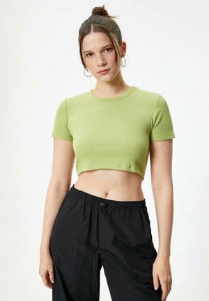 Top de algodón acanalado verde claro, estilo crop, con mangas cortas. El diseño presenta un cuello redondo y una silueta ajustada, combinado con pantalones negros.