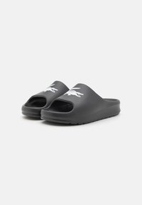 Sandales noires à glissière en caoutchouc avec un design à bout ouvert, arborant un logo de crocodile blanc à l'avant. Semelle texturée pour une meilleure adhérence.