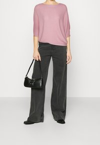 T-shirt court, en tricot lâche, rose pâle, associé à un pantalon large noir taille haute. Sac à main noir avec un fermoir et des chaussures plates.