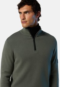 Maglione zip-up verde chiaro con colletto alto, dotato di una cerniera nera e tessuto testurizzato. Maniche lunghe con un design aderente.