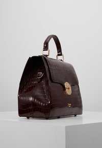 Burgundy faux-krokodil handväska med en strukturerad form, guldhardware och ett handtag upptill. Har en spänne-låsning och en slät textur.