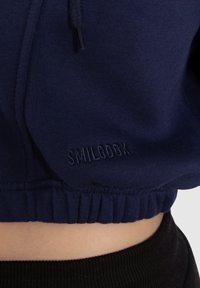 Felpa navy con orlo e polsini a coste, caratterizzata da un logo ricamato "SMILOBOK". Materiale morbido con finitura testurizzata.