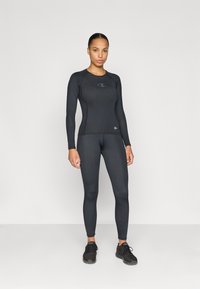 Zwarte lange mouwen sporttop en aansluitende leggings gemaakt van een rekbare, gladde stof, met een klein logo op de borst en bij de enkel.