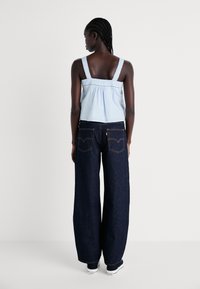 Top sem mangas azul claro com rendas, combinado com calças de ganga escuras de perna larga e ténis pretos. Vista de trás.