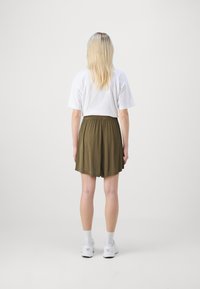 Bílý tričko a olivově zelené šortky s elastickým pasem, vyrobené z texturované látky. Bílé boty jsou viditelné na dně.