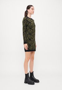 Strikket kjole med svart bunn og grønn leopardmønster, lange ermer og rund hals; stylet med svarte kraftige ankelstøvler.