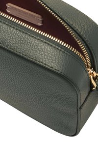 Borsa da trucco in pelle verde con superficie testurizzata, zip dorata e interno bordeaux. Presenta un'etichetta con logo all'interno. Forma compatta e rettangolare.