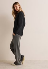 Svart långärmad tröja med en avslappnad passform, kombinerad med gråa lösa byxor och vita sneakers. Slät tyg med minimala designdetaljer.
