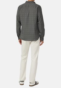 Donker bedrukte shirt met lange mouwen, omklapbare kraag en knoopmanchetten, gecombineerd met witte broek en casual schoeisel.