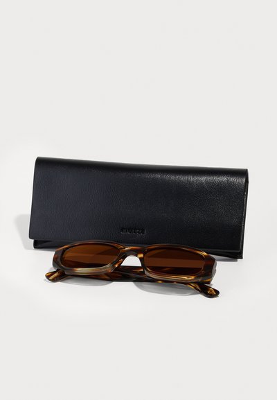 Lunettes de soleil en écaille de tortue avec des verres marron, accompagnées d'un étui en cuir noir texturé. L'étui présente un design minimaliste.