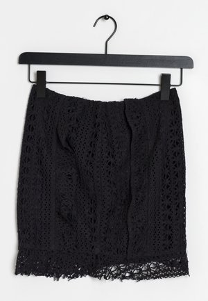 Schwarzer Spitzenrock mit strukturiertem Design, floralem Muster und einem gewellten Saum. Hängt an einem schwarzen Metallkleiderbügel.