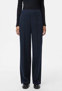 Pantalones de pierna ancha azul marino con rayas blancas verticales, con una cinturilla elástica y una textura suave, combinados con calzado negro.