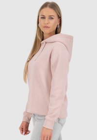 Felpa rosa chiaro con cappuccio, maniche lunghe, polsini a costine e una texture morbida. Design minimalista, abbinata a jeans grigi.