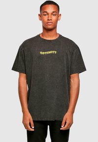 Schwarzes Baumwoll-T-Shirt mit lockerer Passform, Rundhalsausschnitt und gelbem "OPTIMIST"-Text auf der Brust gedruckt.