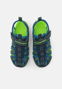 Sandalias Skechers en azul marino y verde con diseño de malla, correas ajustables y suelas blancas, que presentan plantillas verdes texturizadas.