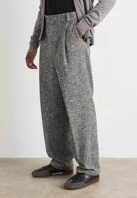 Pantaloni di tweed grigio con finitura strutturata, gamba larga e pieghe davanti, abbinati a scarpe nere con suola marrone.
