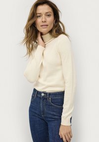Ivory coltrui van zachte stof met lange mouwen, aansluitend ontwerp. Gecombineerd met donkerblauwe high-waisted jeans met een klassieke snit.
