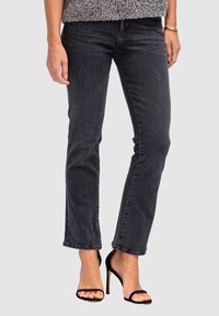 Jean en denim noir avec une coupe droite, un léger délavage et une hem raccourcie, associés à des sandales à talons hauts noires à lanières.