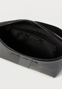 Μαύρο νεσεσέρ Armani Exchange με φερμουάρ, εσωτερική θήκη και ασημί λογότυπο της μάρκας μπροστά, εμφανίζεται ανοιχτό σε λευκό φόντο.