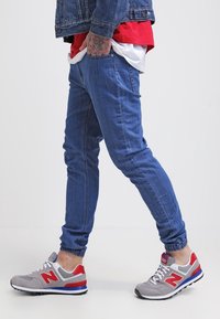 Jeans-joggers i medelblått, tapered fit med elastiska muddar. Matcher med grå och röda New Balance sneakers med en texturerad överdel och gummisula.