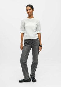 Pull gris clair avec des manches bouffantes texturées et des ourlets côtelés plats. Associé à un jean droit gris foncé et des chaussures noires.