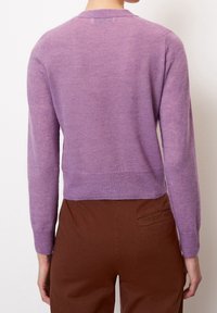 Lila ullblandad tröja med långa ärmar, rund halsringning och cropped passform, kombinerad med bruna byxor och en enkel svart design.