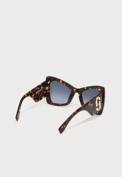 Sonnenbrille aus Schildpatt mit kantigen Rahmen, blauen Gläsern und goldenen Hardware-Akzenten. Die strukturierte Oberfläche verstärkt das visuelle Interesse.