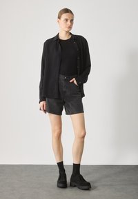 T-shirt noir à manches longues, débardeur noir ajusté, shorts en denim noir taille haute et chaussures à semelle épaisse noires. Design minimaliste, look décontracté.