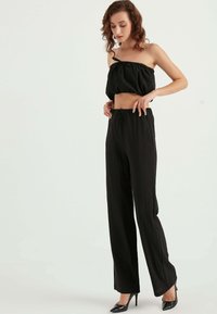 Black two-piece outfit featuring a cropped top with gathered elastic and drawstring pants with a relaxed fit and textured fabric.