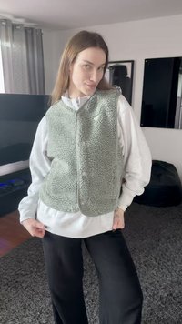 Fleece vest in soft green, featuring a rounded neckline, front buttons, and a textured finish, layered over a white sweatshirt.