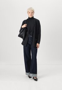 Mörkgrå stickad tröja, lång svart kardigan med fickor, vida splittade mörk denimjeans med uppvikt nederkant, och svarta spetsiga ballerina.