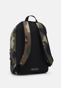 Bakifrån vy av en ryggsäck med kamouflagemönster, utrustad med vadderade svarta axelremmar och ett handtag ovanpå, mot en enkel bakgrund.